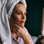 Woman looks at glowing, healthy skin in mirror after a series of Hydrafacial treatments for acne