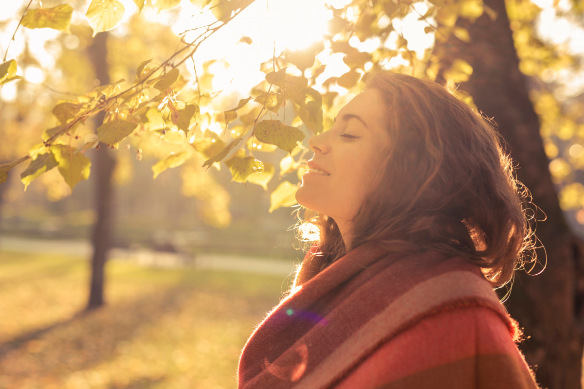 Woman smiling in the sun under fall leaves